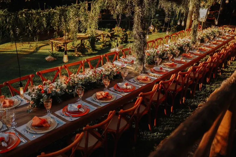 A long candlelit dinner table set outdoors under trees